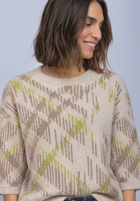 Eine lächelnde Frau mit schulterlangem Haar trägt einen beigen Pullover mit grünem Karomuster.