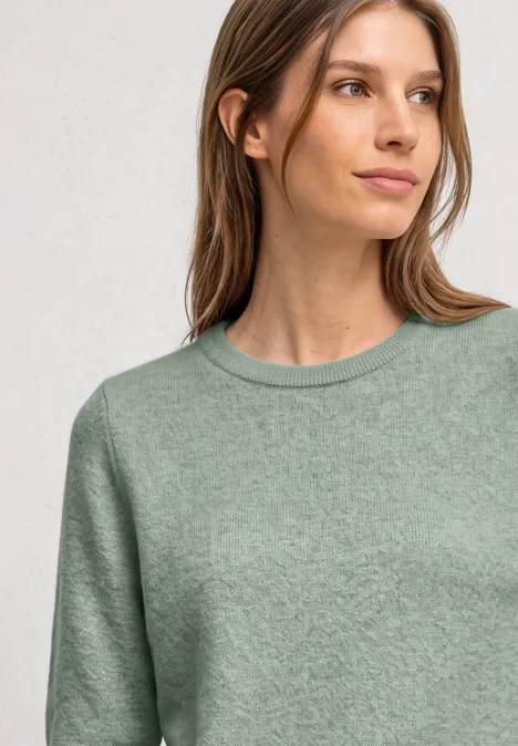 Kurzarm Pullover mit Rundhals und Rüschen eucalyptus green mel. Eine Frau mit langem braunem Haar trägt einen hellgrünen, strukturierten Pullover vor grauem Hintergrund.