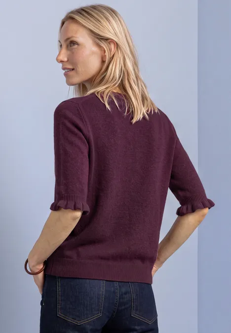 Kurzarm Pullover mit Rundhals und Rüschen berry maroon Frau im Profil trägt bordeauxroten 3/4-Arm-Pullover mit hochgekrempelten Ärmeln und Jeans vor blasser Wand.