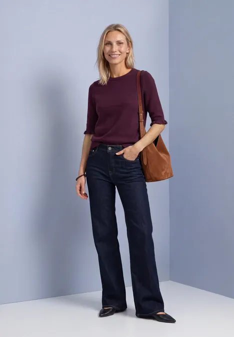 Kurzarm Pullover mit Rundhals und Rüschen berry maroon Eine blonde Frau in bordeauxfarbenem Pullover, weiten Jeans und brauner Tasche vor neutralem Hintergrund.