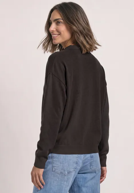 Langarm Pullover mit Polokragen black coffee Frau im dunklen Pullover und Jeans blickt über die Schulter und lächelt vor hellem Hintergrund.