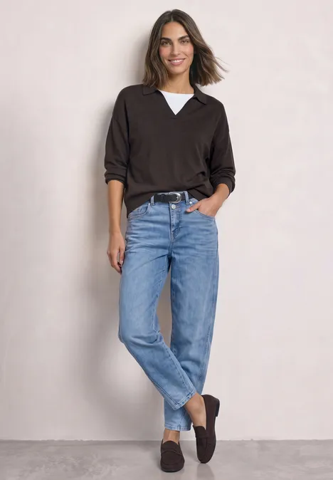 Langarm Pullover mit Polokragen black coffee Frau in schwarzem V-Pullover über weißem Shirt, blauen Jeans und schwarzen Loafers vor hellgrauer Wand.