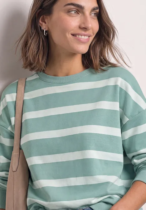 Sweatshirt mit Rundhals und Streifen eucalyptus green Frau mit kurzem braunem Haar, lächelnd, trägt grünen gestreiften Pullover und Umhängetasche.