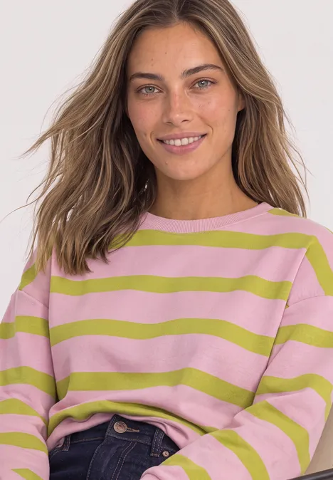 Sweatshirt mit Rundhals und Streifen apple lime Lächelnde Frau mit gestreiftem rosa-grünem Pullover und lockeren Haaren vor hellem Hintergrund.
