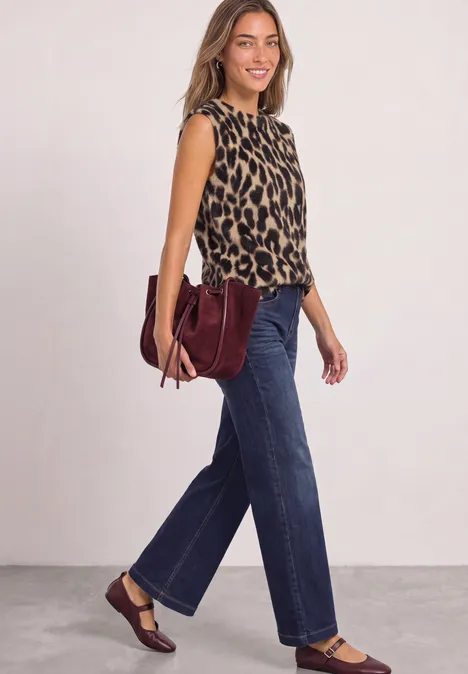 Eine Frau in ärmellosem Leo-Top, weiten Jeans und burgunderfarbener Tasche mit passenden Schuhen.