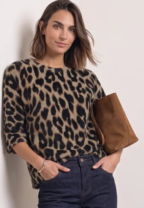 Frau in beige-schwarzem Leo-Pullover, trägt eine braune Tasche und posiert vor hellem Hintergrund.