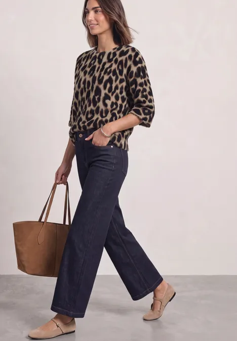 Moderne Frau in Leopardenpullover, weitem Jeans, beigen Absätzen und großer brauner Tasche.
