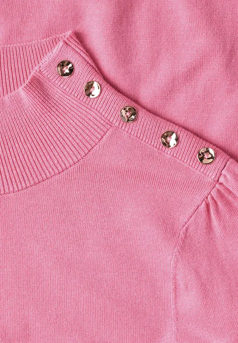 Roze gebreide trui met opvallende gouden knopen op de schouder.