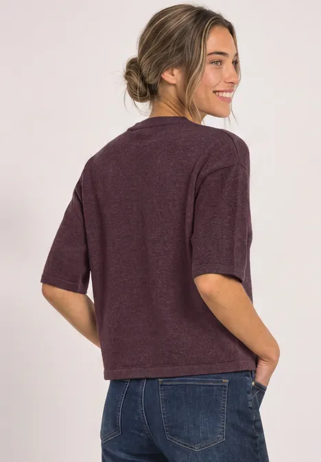 Pull à manches 3/4 et col rond rustic rouge mel. Frau mit Dutt im bordeauxfarbenen Kurzarm-Pullover und Jeans, seitlich lächelnd.