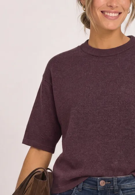 Pull à manches 3/4 et col rond rustic rouge mel. Frau mit weinrotem T-Shirt und Jeans, lächelt, hält braune Tasche.
