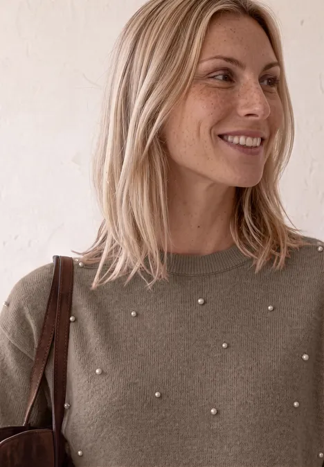 3/4-Arm Pullover mit Rundhals sanded amber mel. Eine blonde Frau mit Perlen-Verzierung am Pullover trägt eine Tasche und lächelt sanft seitlich.