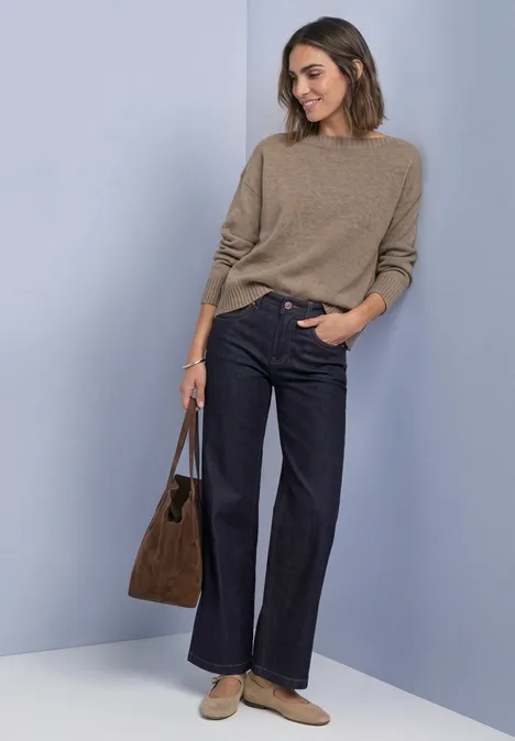 Langarm Pullover mit Boat Neck sanded amber mel. Frau trägt beigen Pullover, dunkelblaue Schlaghose und braune Tasche vor neutralem Hintergrund.