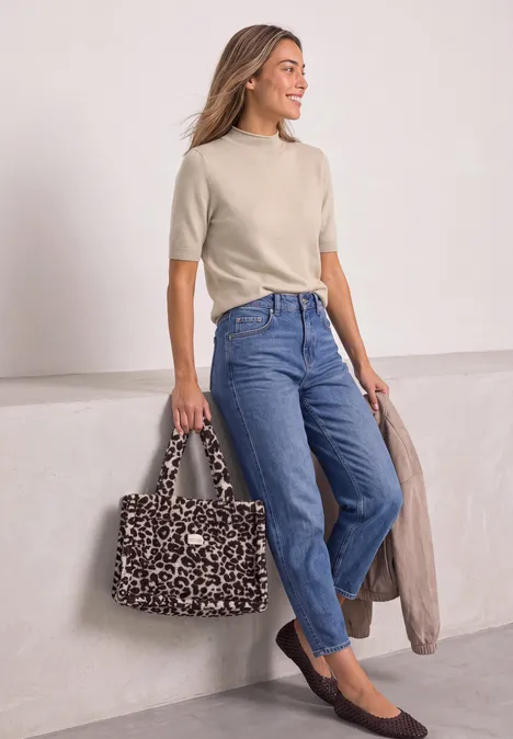 Frau trägt beige T-Shirt, blaue Jeans, schwarze Ballerinas, hält gepunktete Leo-Handtasche