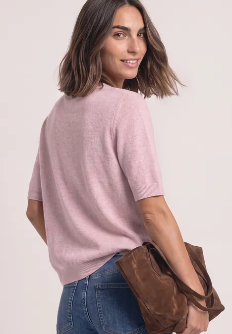 Frau im rosa Kurzarm-Pullover und blauen Jeans, lässig mit einer braunen Tasche in der Hand.