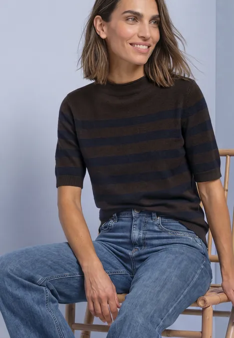 Frau in gestreiftem Pullover und blauer Jeans auf Holzstuhl sitzend.