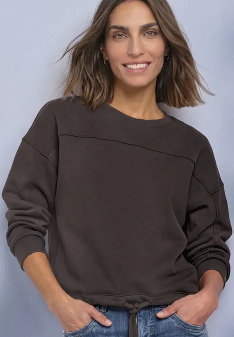 Sweat-shirt à col rond avec détails décoratifs black coffee Frau mit lässigem Pullover in dunkler Farbe, leicht lächelnd vor neutralem Hintergrund.