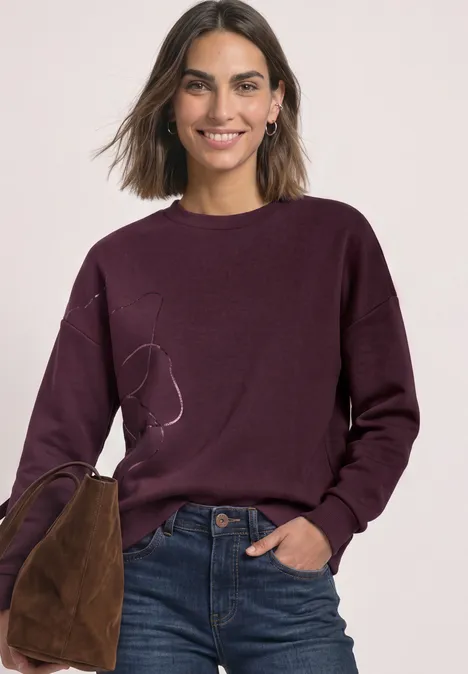 Sweatshirt met Loose Fit-pasvorm en folieprint rustic rouge Frau in lila Pullover und Jeans mit brauner Tasche, lächelt.