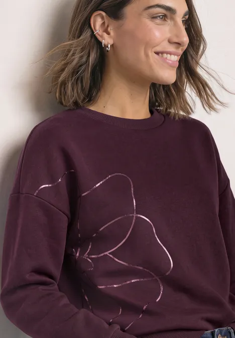 Sweatshirt met Loose Fit-pasvorm en folieprint rustic rouge Frau lächelt seitlich in einem burgunderfarbenen Pullover mit dezentem Blumenlinienmuster.