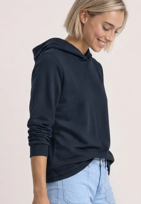 Langarm Sweatshirt mit Kapuze darkest blue Eine Frau in dunkelblauem Hoodie und hellblauen Hosen lächelt seitlich.