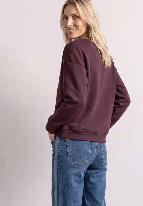 Femme en sweat violet et jean se retourne en souriant.