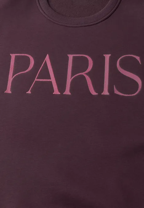 Gros plan d'un sweat bordeaux avec l'inscription 'PARIS' en lettres roses.