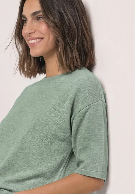 Frau lächelt seitlich in lockerem grünen T-Shirt mit kurzen Ärmeln.