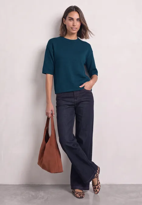 3/4-Arm Pullover mit Rundhals blue petrol mel. Eine Frau trägt ein petrolfarbenes T-Shirt, dunkelblaue Schlagjeans, Leo-Ballerinas und hält eine braune Tasche.