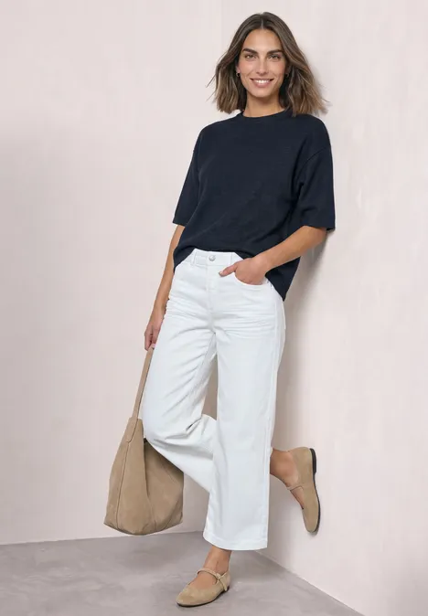 3/4-Arm Pullover mit Rundhals darkest blue mel. Eine lächelnde Frau lehnt an heller Wand, trägt navy T-Shirt, weiße Hose, beige Tasche und passende Schuhe.