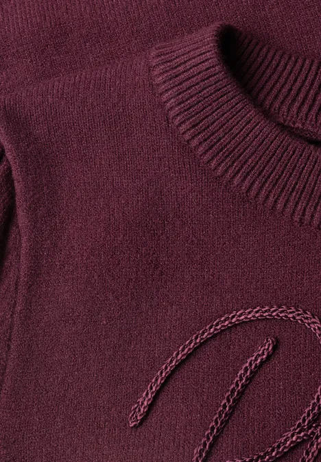 Gros plan d’un pull en maille bordeaux à col rond avec texture fine.