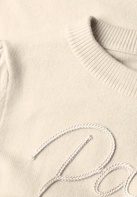 Gros plan sur un pull crème à col côtelé avec broderie cursive argentée