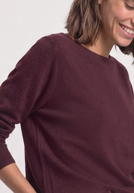 Eine lächelnde Frau trägt einen bordeauxfarbenen Pullover im Halbprofil.