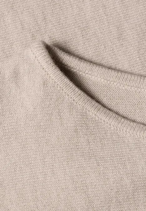 Close-up van beige gebreide stof met een gestikte rand.