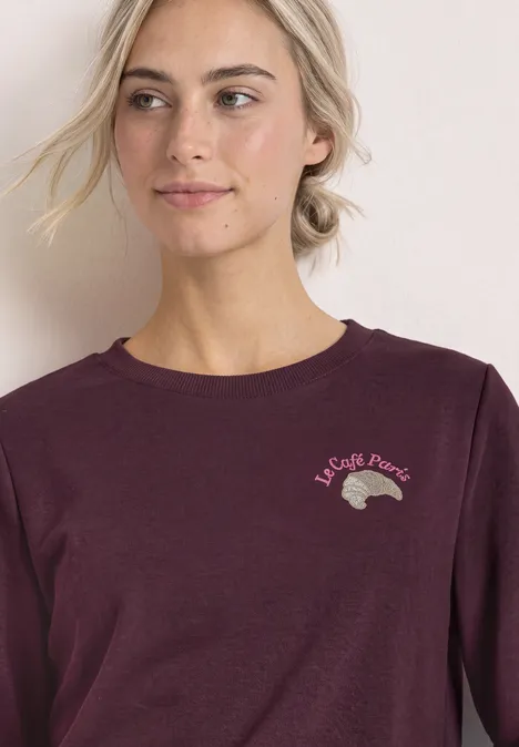 Frau in dunkelrotem Langarmshirt mit kleinem Igel-Print und französischem Schriftzug.
