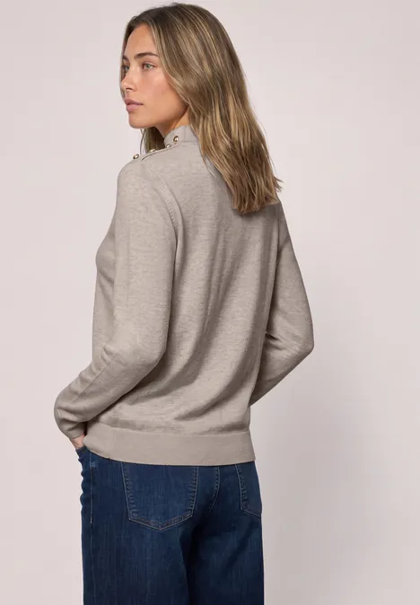 Frau von hinten in hellgrauem Pullover und blauer Jeans, schaut seitlich, neutraler Hintergrund.