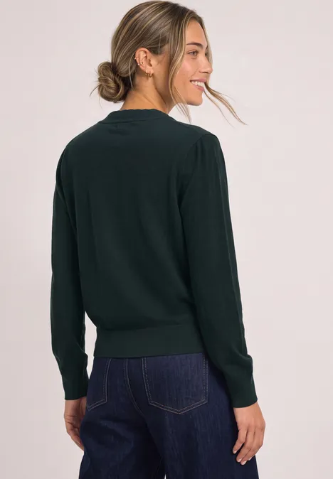 Een vrouw draagt een donkergroene trui en jeans, lachend kijkt ze over haar schouder.