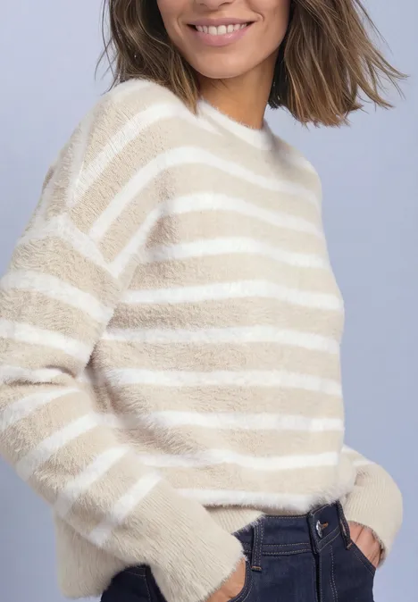 Eine Frau trägt einen creme-weiß gestreiften, flauschigen Pullover, lässig in dunkle Jeans gesteckt.