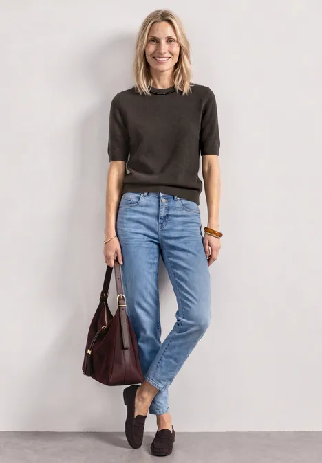 Frau in lässigem Outfit: schwarzes Kurzarmshirt, blaue Jeans, schwarze Loafers und eine bordeauxrote Handtasche.
