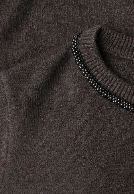 Nahaufnahme eines dunkelbraunen Strickpullovers mit schwarzer Perlenverzierung am Rundhalsausschnitt.