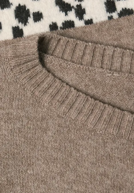 Gros plan sur un pull en maille brun clair à col rond, posé sur un tissu à motif blanc et noir.
