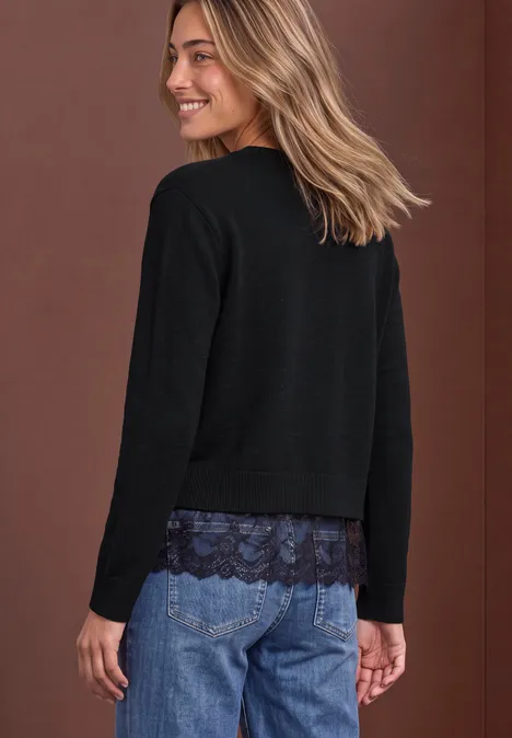 Pullover mit Rundhals und Spitzenkante Black Frau im Profil in Jeans und schwarzem Pullover mit Spitzenbesatz, lächelnd vor braunem Hintergrund