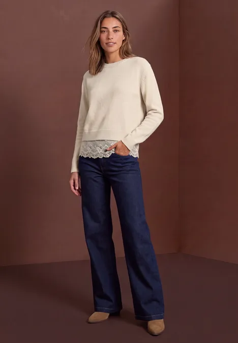 Pullover mit Rundhals und Spitzenkante pure beige Ein Model trägt einen hellen Pullover mit Spitzenbesatz und weite dunkelblaue Jeans.