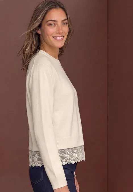 Pullover mit Rundhals und Spitzenkante pure beige Frau in beigem Pullover mit Spitzenabschluss und Jeans, lächelnd vor braunem Hintergrund.