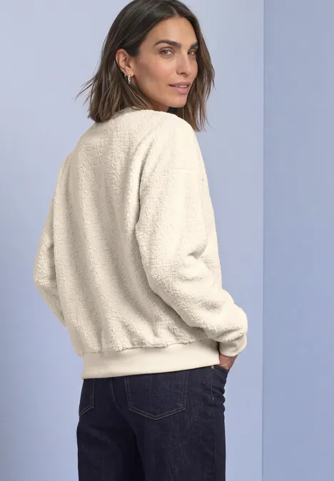 Teddy-Sweatshirt mit Zipperdetails pure beige Frau trägt cremefarbene Teddy-Jacke und Jeans, schaut über die Schulter, vor neutralem Hintergrund.