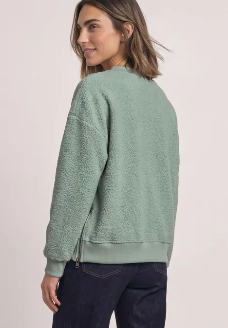 Teddy-Sweatshirt mit Zipperdetails eucalyptus green Seitliche Ansicht einer Frau in grünem Teddy-Fleece-Sweatshirt und dunklen Jeans vor hellem Hintergrund.