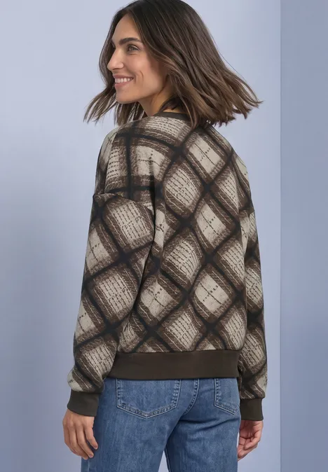 Femme souriante en pull à carreaux et jeans, regardant de côté.