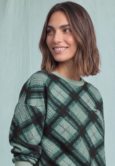 Sweat-shirt à col rond et motif à carreaux stormy green Une femme souriante portant un pull vert à carreaux devant un fond clair.