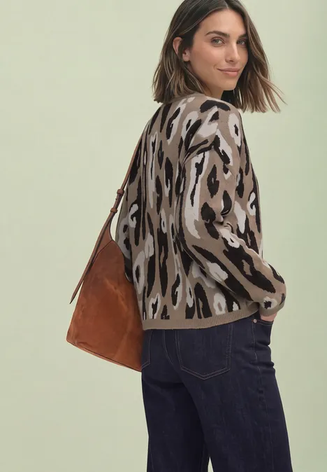 Frau mit Leopardenmuster-Pullover, dunklen Jeans und brauner Wildledertasche, schaut über die Schulter.