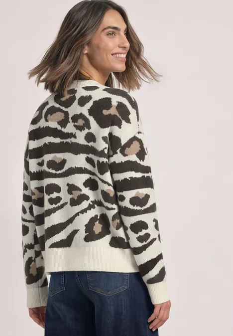 Femme en jeans et pull beige à imprimé animal, souriante de profil.