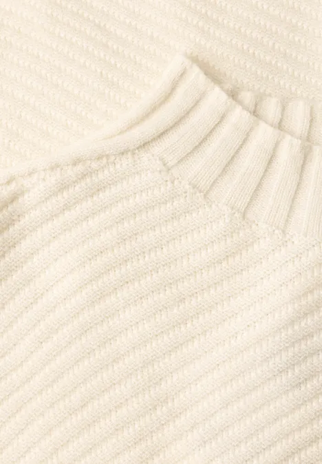 Nahaufnahme eines cremefarbenen Strickpullovers mit diagonaler Rippenstruktur und geripptem Kragen.