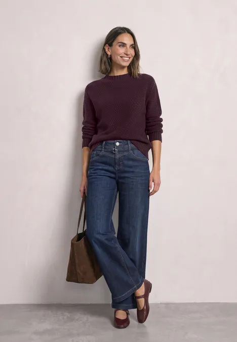 Langarm Pullover mit Turtle Neck und Struktur berry plum Frau in lila Pullover, weitem Jeans und braunen Loafers mit passender Tasche.
